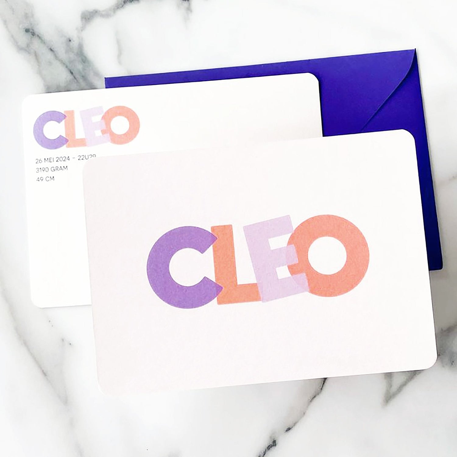 Geboortekaartje met de naam CLEO prominent afgebeeld in grote, pastelkleurige blokletters, variërend in roze en paars. De kaart is strak en minimalistisch vormgegeven met afgeronde hoeken. Het bijpassend envelopje is een opvallend paarse kleur, wat mooi contrasteerd met de kaart.