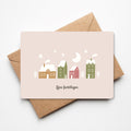 Kerstkaart met illustratie van sfeervolle winterhuisjes in een minimalistische stijl, liggend op een bruine envelop.