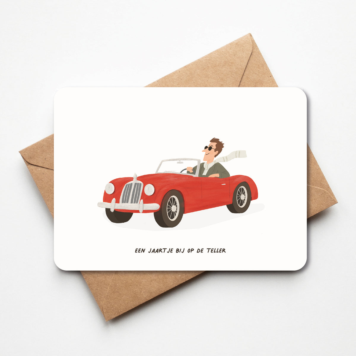 Verjaardagskaart met een man in een rode oldtimer en de tekst ‘Een jaartje bij op de teller’, met afgeronde hoeken op een kraftenvelop.